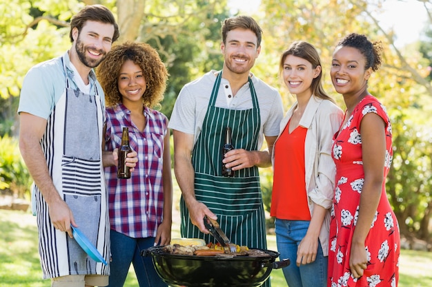 Porträt von den glücklichen Freunden, die einen Grillgrill im Park vorbereiten