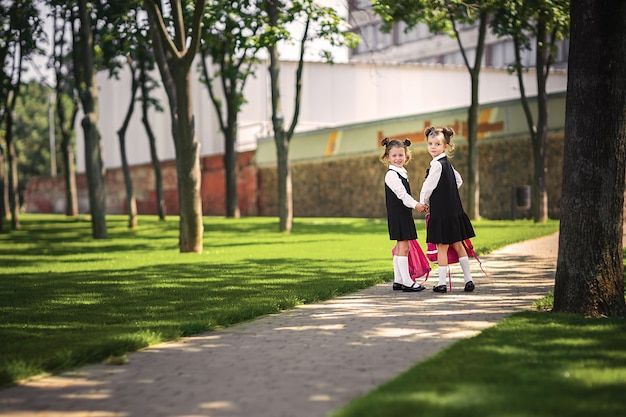 Porträt von den glücklichen kaukasischen jungen lächelnden Mädchen, die Schulrucksack außerhalb der Grundschule tragen.