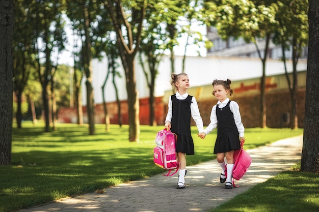 Porträt von den glücklichen kaukasischen jungen lächelnden Mädchen, die Schulrucksack außerhalb der Grundschule tragen.