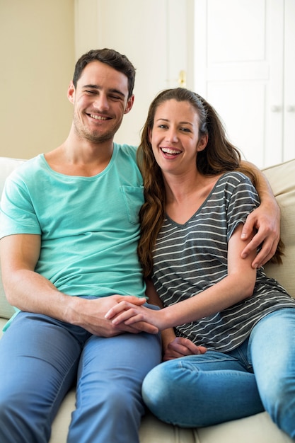 Porträt von den jungen Paaren, die auf Sofa im Wohnzimmer sitzen