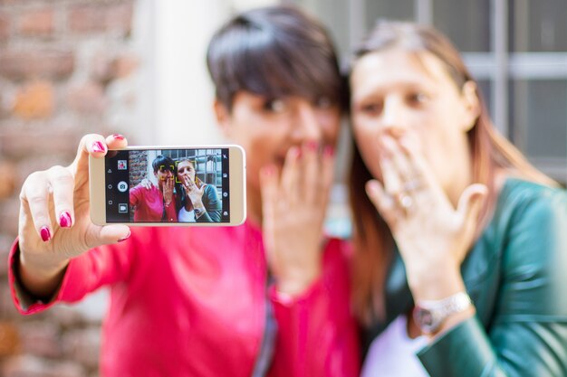 Porträt von den schönen jungen Frauen, die selfie in der Stadt mit einem Smartphone tun