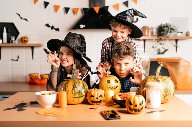 Porträt von drei Kindern, die sich während der Halloween-Party unterhalten, während sie in einem dekorierten Raum am Tisch stehen
