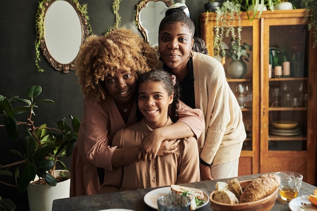 Porträt von drei Schwestern, die sich umarmen und in die Kamera lächeln, während sie beim Familienessen am Tisch sitzen