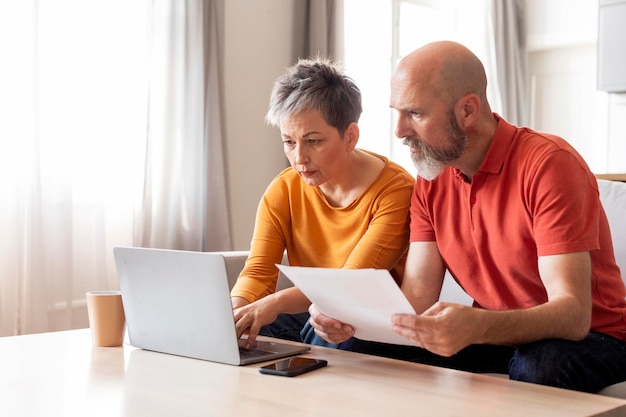 Porträt von ernsthaften reifen Ehegatten mit Laptop, die zusammen Papierarbeit erledigen