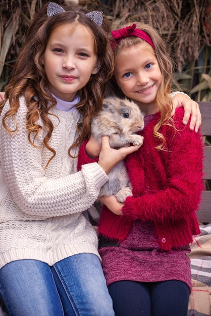 Porträt von Freundinnen kleiner Mädchen im Herbst mit einem Kaninchen in den Händen in der Nähe ihrer Hausfamilie