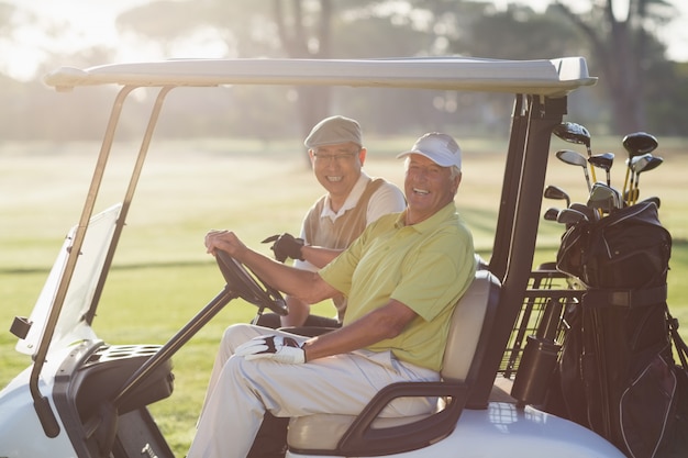 Porträt von fröhlichen Golferfreunden, die im Golfbuggy sitzen