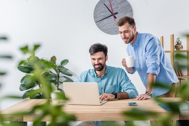 Porträt von Geschäftskollegen, die mit Laptop am Arbeitsplatz im Büro arbeiten