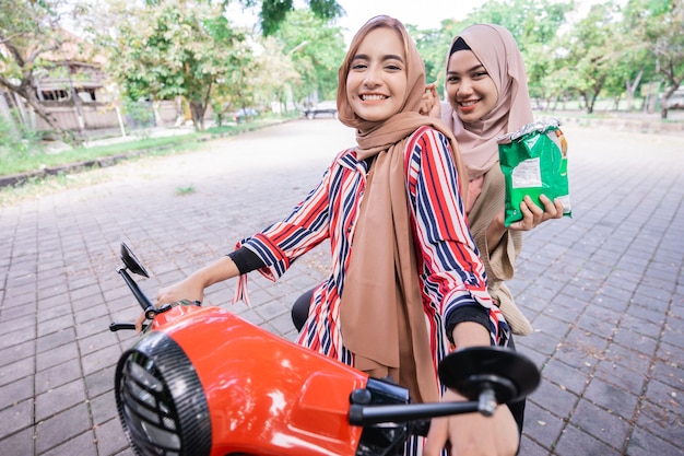Porträt von glücklichen muslimischen Mädchen, die Roller fahren, genießen Sommerferien mit Freunden