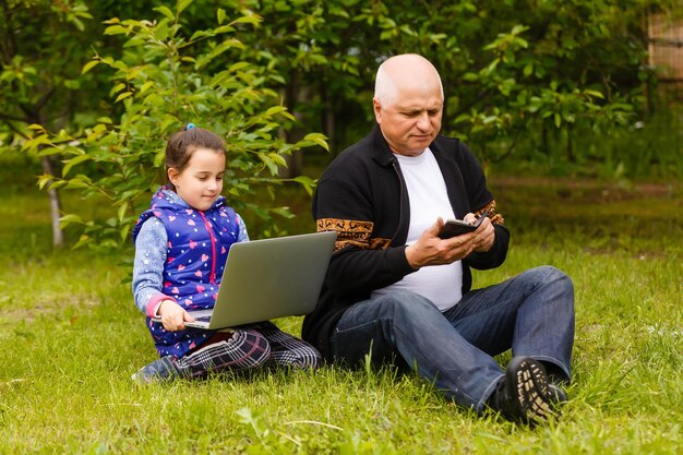 Porträt von Großvater und Enkelin, die Hausaufgaben mit Laptop machen.