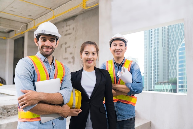 Porträt von jungen asiatischen und kaukasischen Ingenieuren Teamwork Baustelleninspektor und diskutieren gemeinsam mit Notebook-Computer und Papier Blaupause auf der Baustelle Hausrenovierung Ideen Konzept