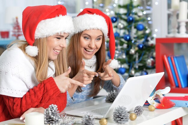 Porträt von jungen lächelnden Frauen in Weihnachtsmützen mit Laptop