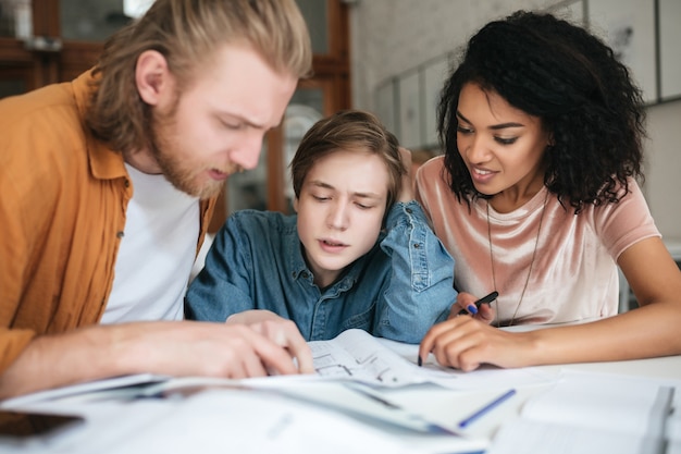 Porträt von jungen Leuten, die nachdenklich etwas im Amt besprechen. Zwei Jungen mit blondem Haar und Mädchen mit dunklem lockigem Haar arbeiten an neuem Projekt im Klassenzimmer