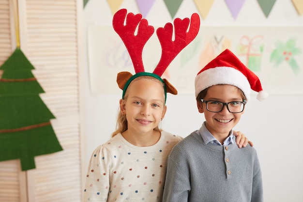 Porträt von Jungen und Mädchen, die Weihnachtsmützen tragen und Kamera betrachten, während Klasse an Weihnachten genießen, Raum kopieren