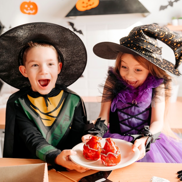 Porträt von Kindern in Halloween-Kostümen, die Süßigkeiten und Snacks essen, während sie in der dekorierten Küche feiern