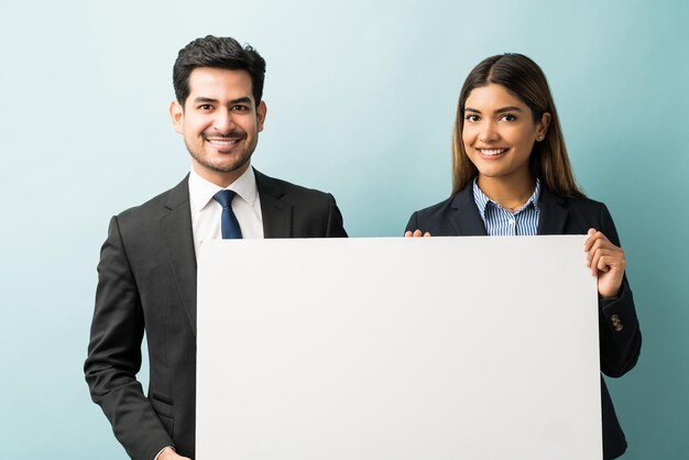 Porträt von lächelnden Führungskräften der Wirtschaft, die ein leeres Plakat halten, während sie vor blauem Hintergrund stehen