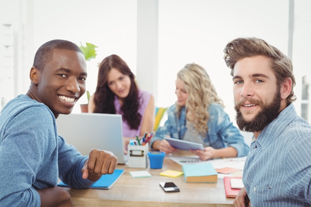 Porträt von lächelnden Geschäftsleuten mit den Frauen, die an Hintergrund am Schreibtisch arbeiten