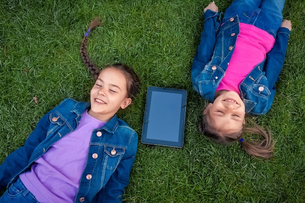 Porträt von lächelnden Mädchen, die mit digitalem Tablet auf Gras liegen