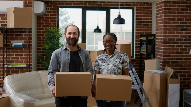 Porträt von Mann und afroamerikanischer Frau, die zusammen in eine neue Mietwohnung ziehen. Halten von Kartons zum Auspacken und Vorbereiten von Immobilien für den Umzug, Haushaltshypothek.