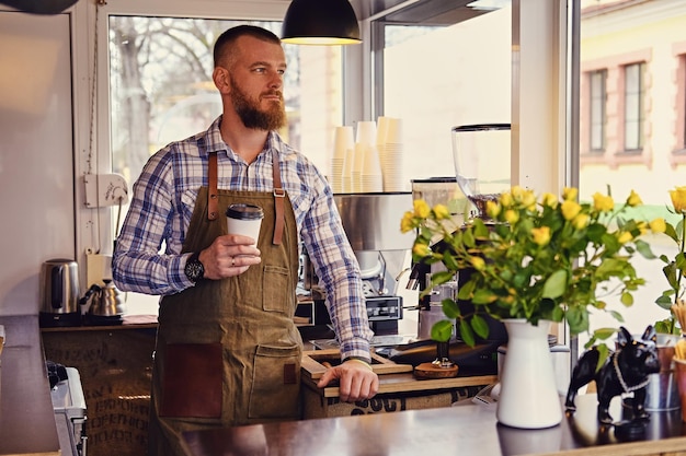 Porträt von Rothaarigen Craft Coffee Verkäufer hält ein Glas Kaffee in einem kleinen Straßencafé.