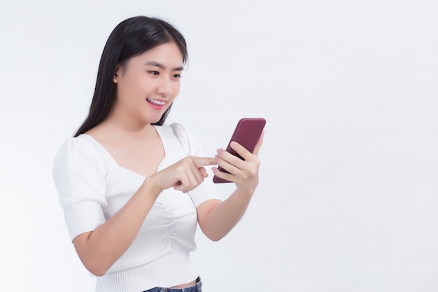 Porträt von schönen asiatischen Frauen Verwenden Sie das Mobiltelefon glücklich an einer weißen Wand