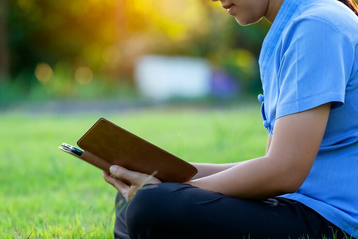 Porträt von schönen jungen Frauen, die sich entspannen, indem sie die Tablette im Rasen aufpassen, entspannen sich.