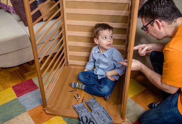 Porträt von Vater und Sohn, die zusammen Kinderbett für ein Neugeborenes zu Hause zusammenbauen. Familienfreizeitkonzept