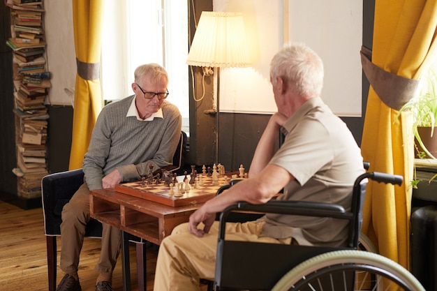 Porträt von zwei älteren Männern, die Schach spielen und Aktivitäten im gemütlichen Pflegeheim genießen
