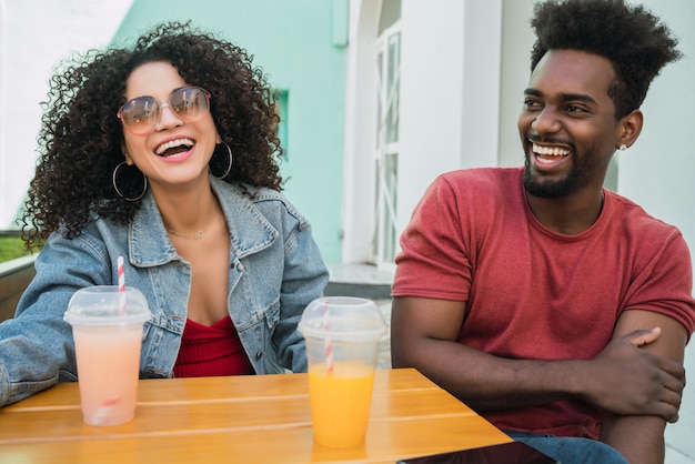 Porträt von zwei Afro-Freunden, die Spaß zusammen haben und gute Zeit genießen, während sie frischen Fruchtsaft draußen in der Cafeteria trinken.