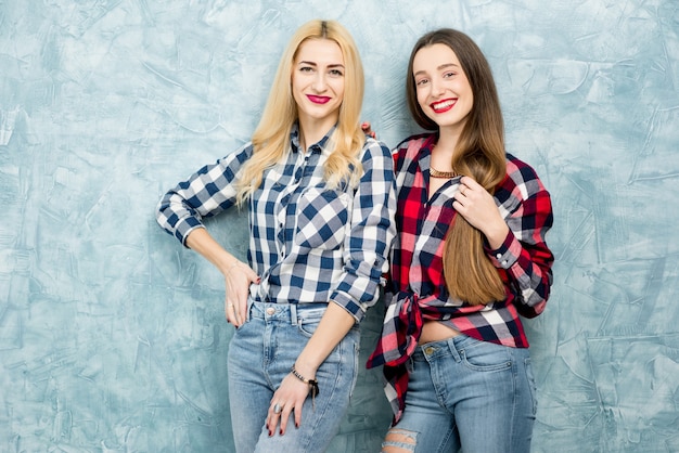 Porträt von zwei Freundinnen in karierten Hemden und Jeans, die zusammen Spaß auf dem blau bemalten Wandhintergrund haben