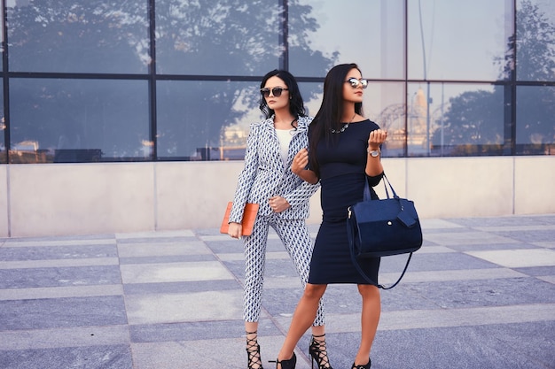 Porträt von zwei Geschäftsfrauen in stilvoller formeller Kleidung, die in einer Innenstadt vor dem Hintergrund eines Wolkenkratzers stehen.
