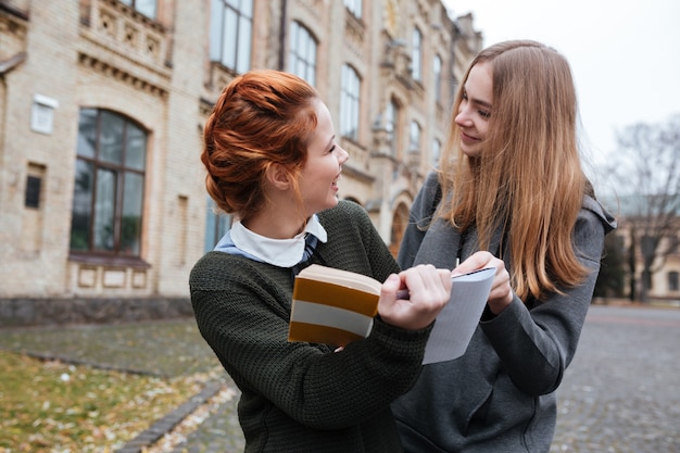 Porträt von zwei glücklichen mädchen, die zusammen auf dem universitätscampus ein buch lesen