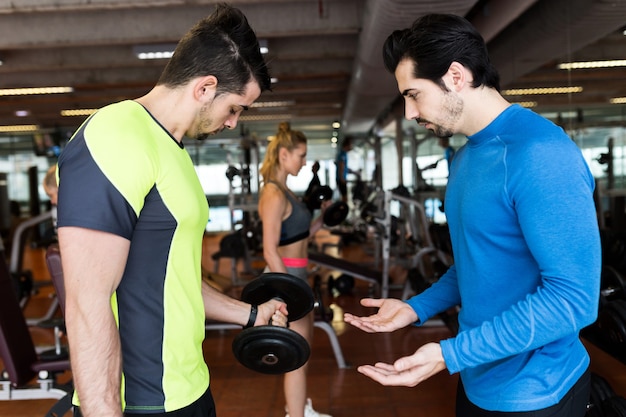 Porträt von zwei gutaussehenden jungen Männern, die Muskelübungen im Fitnessstudio machen.