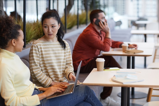 Porträt von zwei jungen Frauen, die zusammenarbeiten, während sie im Café oder Food Court am Tisch sitzen