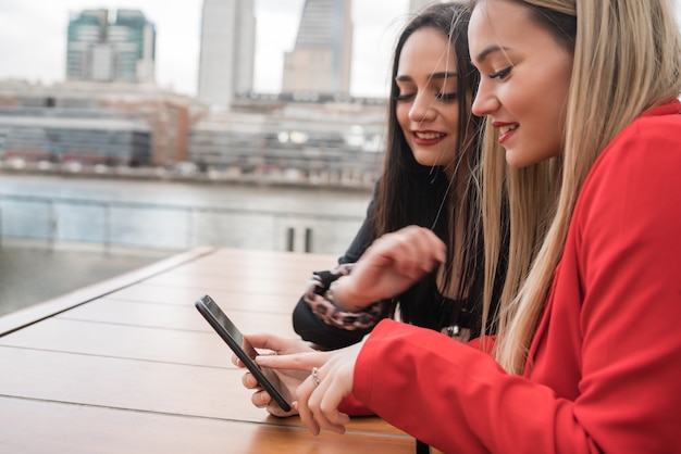 Porträt von zwei jungen Freunden, die ihr Handy beim Sitzen im Café verwenden. Lebensstil- und Freundschaftskonzept.