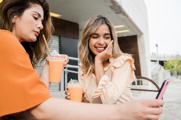 Porträt von zwei jungen Freunden, die ihr Handy in einem Café im Freien benutzen