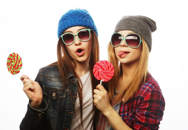 Porträt von zwei jungen hübschen Hipster-Mädchen mit Hüten und Sonnenbrillen, die Süßigkeiten in der Hand halten.