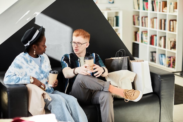 Porträt von zwei jungen Leuten, die sich in der Lounge der Bibliothek unterhalten und Kaffee trinken