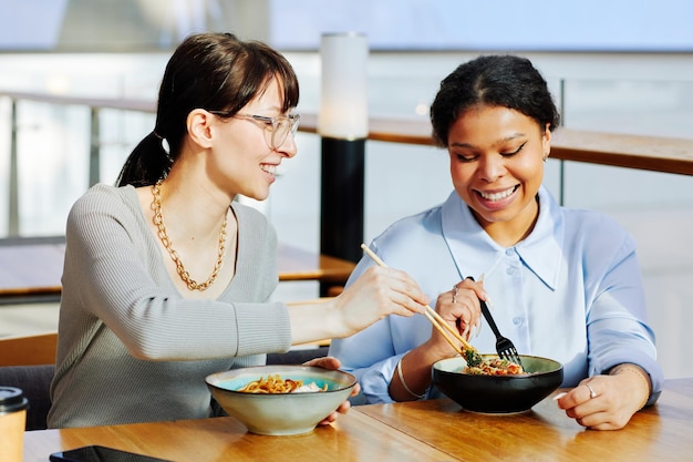 Porträt von zwei jungen Mädchen, die asiatisches Essen im Café genießen und das Essen glücklich lächelnd teilen