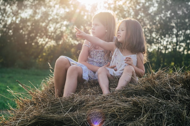 Porträt von zwei Kindermädchen, die auf Strohballen im Heufeld sitzen, zeigen und schauen in die gleiche Richtung Freunde Konzept