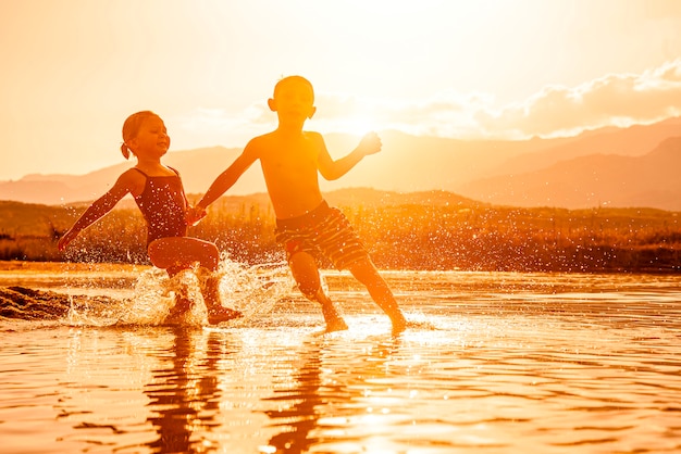 Porträt von zwei Kindern im Alter von 3 und 6 Jahren, die im Meer spielen und Wasser um sie sprühen.