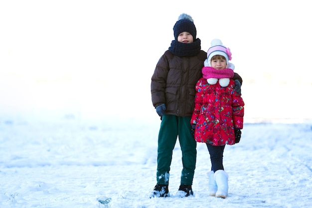 Porträt von zwei Kindern, Jungen und Mädchen, die draußen am verschneiten Wintertag spielen