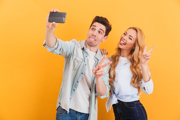 Porträt von zwei lustigen Menschen Mann und Frau, die Selfie-Foto auf Smartphone nehmen, während Siegeszeichen zeigen