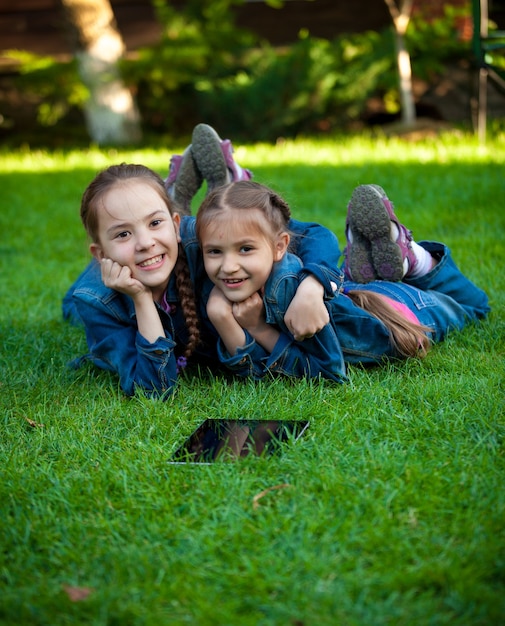 Porträt von zwei Mädchen, die Spaß auf Gras mit Tablet haben