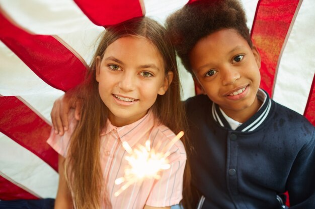 Porträt von zwei niedlichen Mädchen, die funkelnde Lichter halten und auf USA-Flagge lächeln