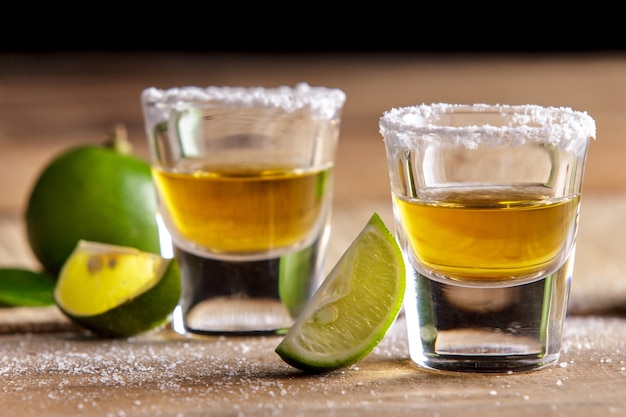 Porträt von zwei Tequila-Aufnahmen mit Limettenscheibe und Salz auf Holztisch