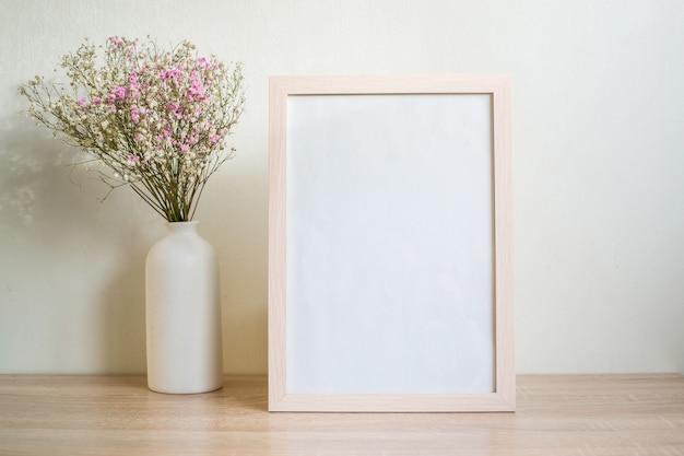 Porträt weißes Bilderrahmenmodell auf Holztisch. Moderne Keramikvase mit Gypsophila.