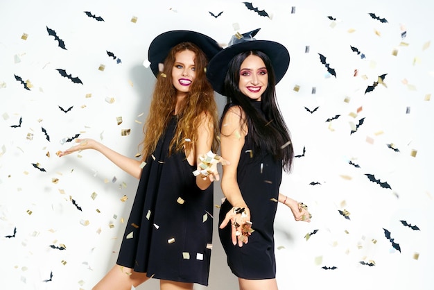 Porträt zweier glücklicher junger Frauen in schwarzen Hexen-Halloween-Kostümen, Feuerwerkskörper im Hintergrund
