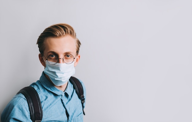 Porträtaufnahme des jungen Mannes, Student mit Rucksack trägt transparente Brille und medizinische Einwegmaske