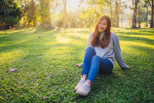 Porträtbild einer schönen asiatischen frau, die vor sonnenuntergang unter natur im park sitzt