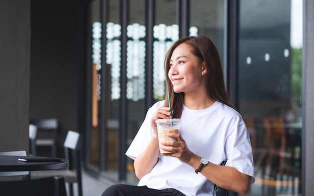 Porträtbild einer schönen jungen asiatischen Frau, die Eiskaffee im Café hält und trinkt